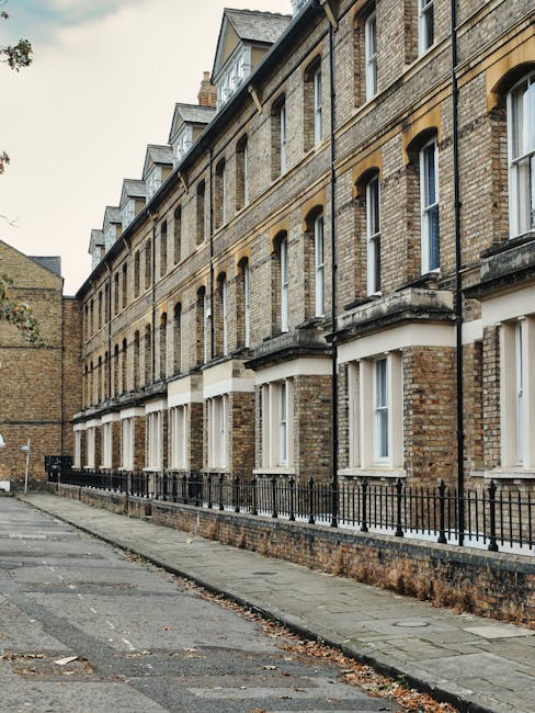 A row of Victorian terrace houses in pastel colours, including shades of yellow, blue, purple, and cream, with large bay windows and decorative mouldings. The houses are located on a street with a low